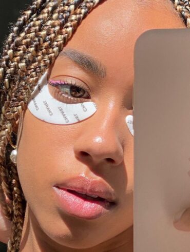 Mulher jovem de pele negra em foto no espelho com material de skin care no rosto.