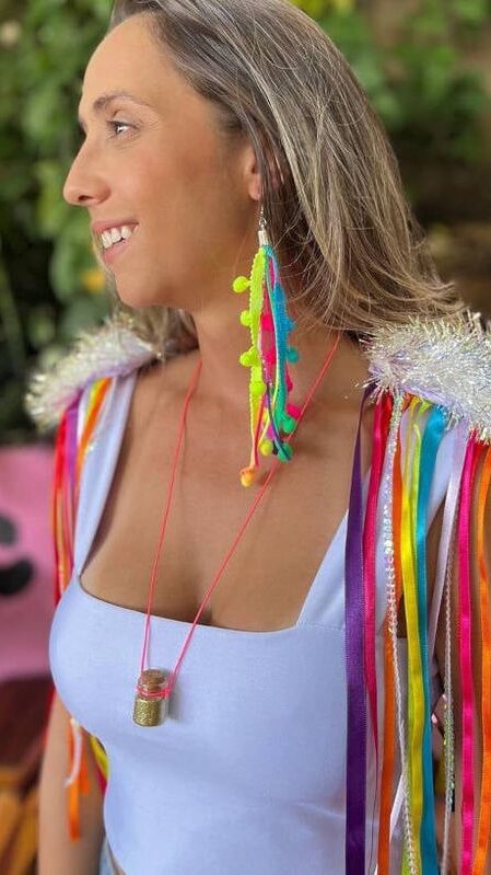 Mulher jovem e magra de pele clara. Ela está usando body branco e ombreiras coloridas.