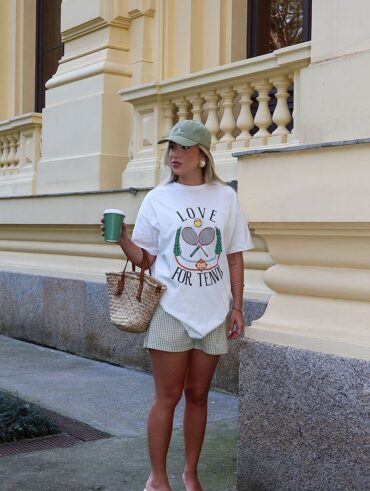 Mulher jovem, loira e magra. Ela veste camiseta estampada branca, bermuda e salto alto.