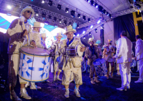 Bateria de escola de samba com homens vestidos de branco e dourado