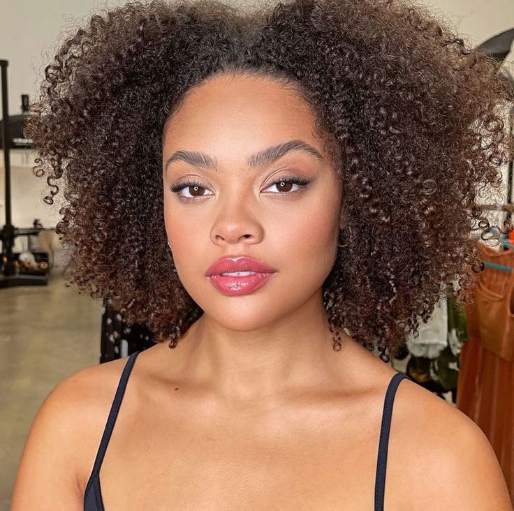 Mulher de pele preta, com regata preta, maquiagem suave e cabelo crespo com corte choppy bob
