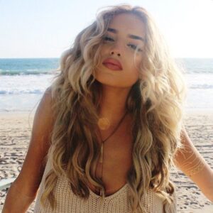 Mulher de pele clara, com blusa clara, cabelo ondulado loiro, na praia