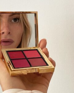 Mulher de pele clara e cabelo loiro, segurando uma paleta de blush dourada