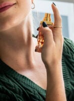 Mulher de pele clara, com suéter verde, espirrando perfume