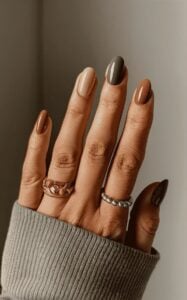 Mão de pele clara, com acessórios em prata e dourado e unha amendoada degradê em tons terrosos