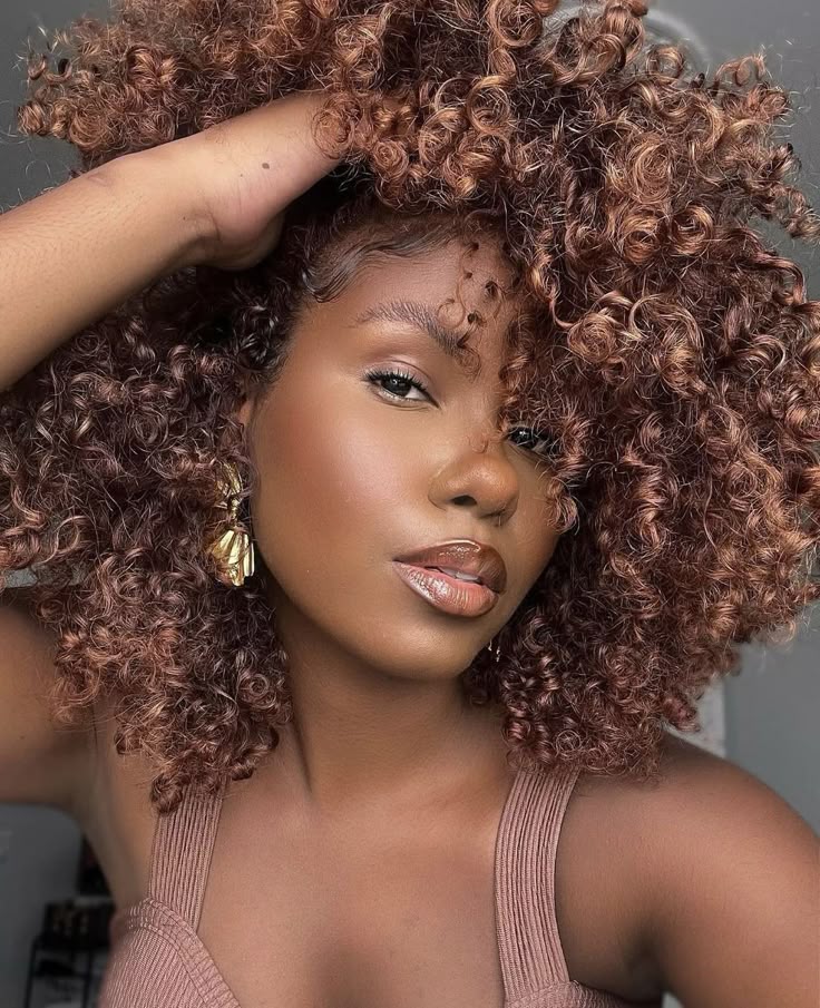 Mulher de pele preta, com regata marrom, cabelo crespo chocolate, acessório em dourado e maquiagem com contorno labial marrom 