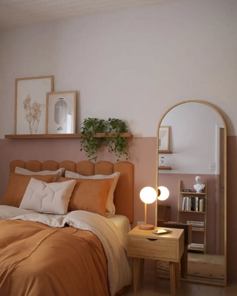 Quarto com cabeceira estofada, prateleira com quadros e planta, espelho oval