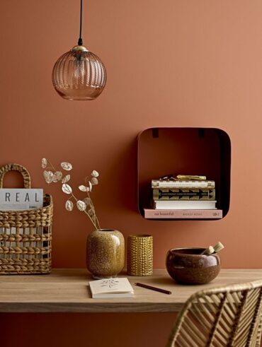 Parede terracota com nicho, mesa e objetos decorativos na mesma paleta