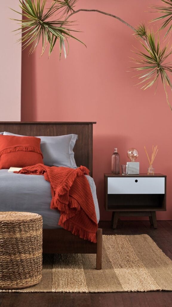 Quarto com parede em rosa-queimado, cama em madeira escura e tapete listrado