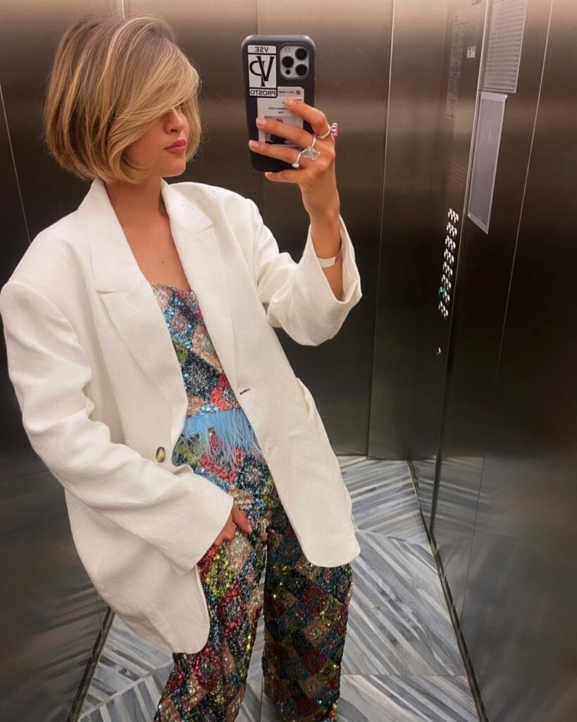 Mulher de pele clara, com macacão colorido, blazer branco e cabelo loiro cup bob