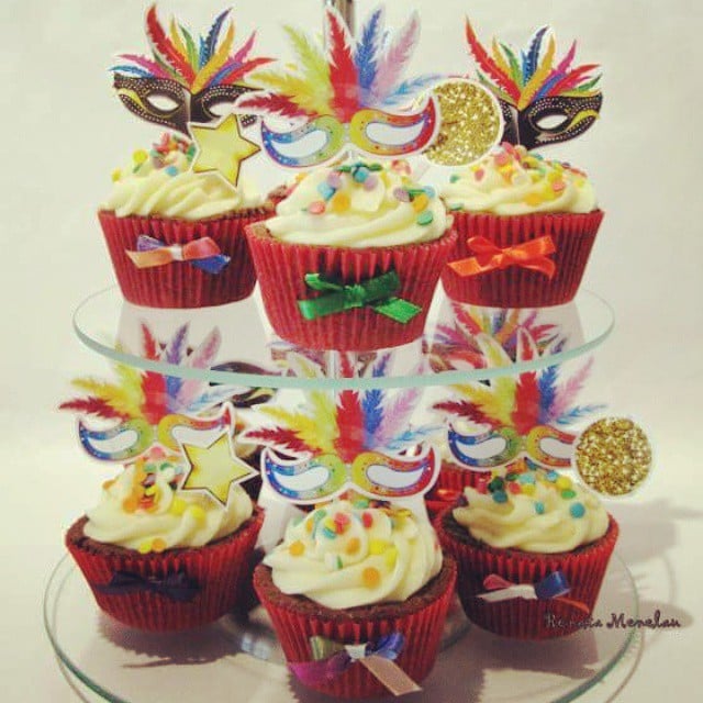 Cupcakes em forminhas vermelhas decorados com confetes e máscaras de carnaval