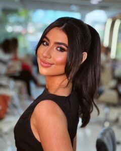 Giulia Albuquerque, com vestido preto, cabelo preto amarrado e maquiagem bronzeada