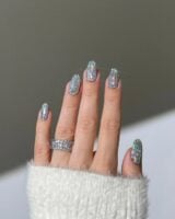 Mão de pele clara, com anel de brilhando e unha amendoada com glitter estilo disco ball