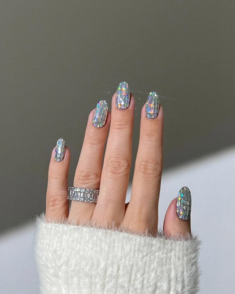 Mão de pele clara, com anel de brilhando e unha amendoada com glitter estilo disco ball