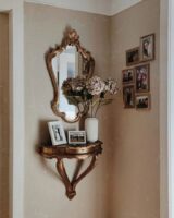 Espelho provençal dourado em cima de uma prateleira pequena com fotos e flores