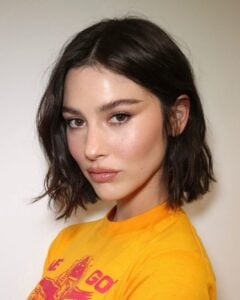 Gracie Abrams, com camiseta amarela, maquiagem simples e corte de cabelo bob