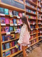 Mulher de pele clara, com cabelo castanho, casaco branco, em uma livraria