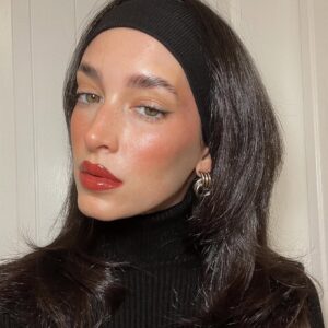 Tori Monet, com cabelo escuro, faixa como acessório, blusa preta e berry makeup