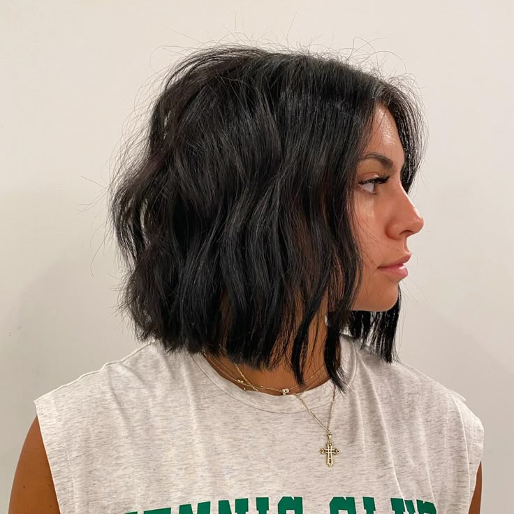 Mulher de pele clara, com regata cinza e cabelo preto com corte choppy bob