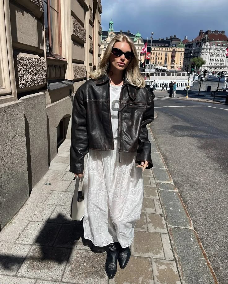 Mulher de pele clara, com cabelo loiro, blusa branca, saia de renda, jaqueta de couro oversized e bota 