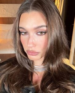 Hailey Bieber, com cabelo castanho médio, acessórios em prata e maquiagem latte