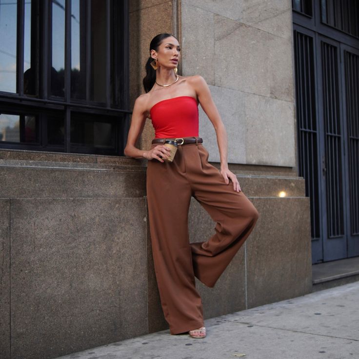 Mulher de pele clara, com top ombro a ombro vermelho, calça Mocha Mousse e cinto preto 