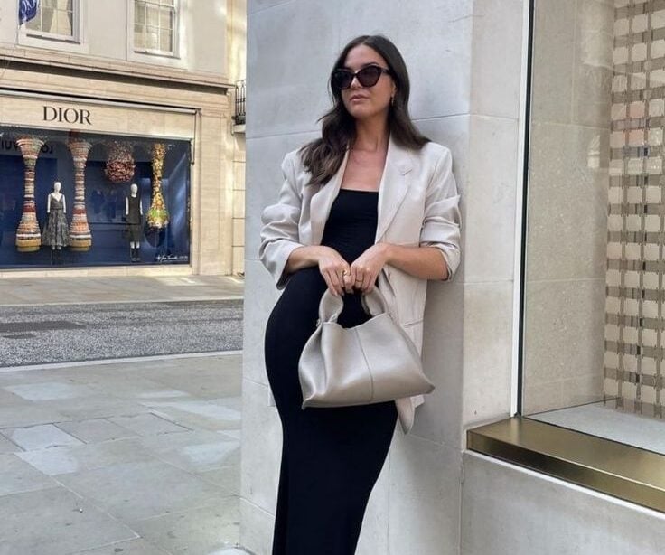 Mulher de pele clara, com blazer e bolsa neutro e chinelo de dedo