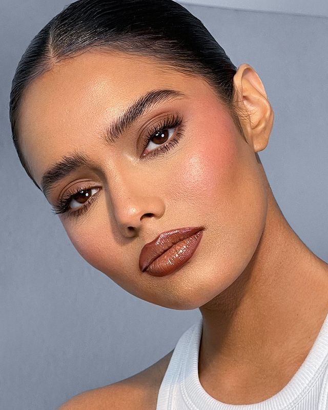Mulher de pele clara, com regata branca, cabelo escuro preto, maquiagem em tons terrosos com gloss marrom 