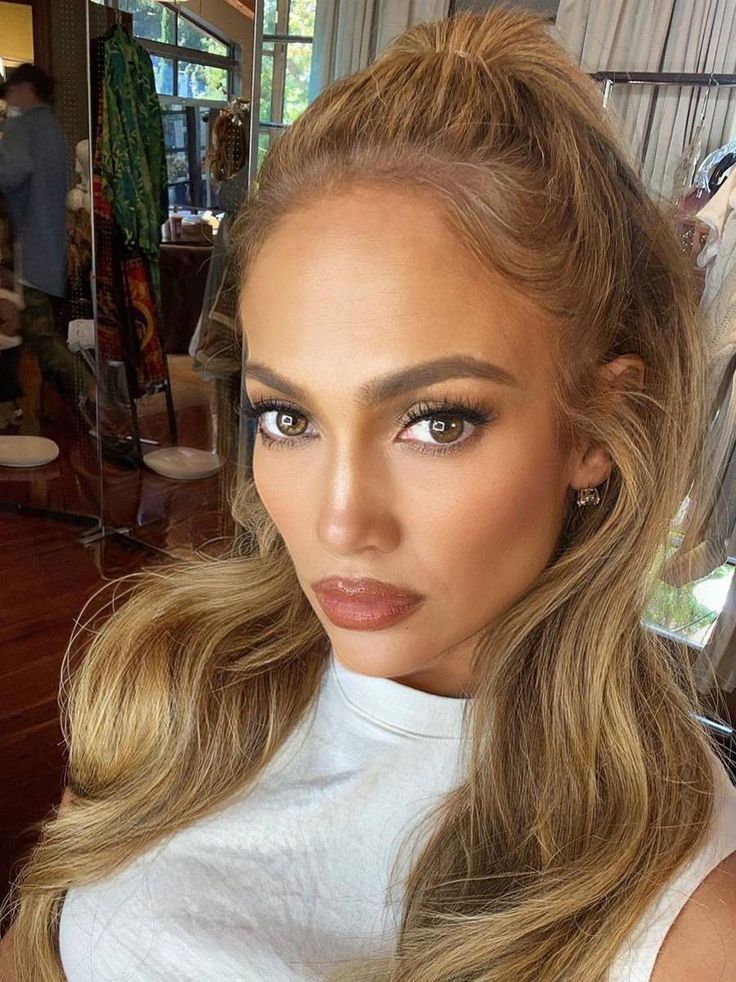 Jennifer Lopez, com blusa branca, cabelo loiro meio preso e maquiagem minimalista com batom marrom 