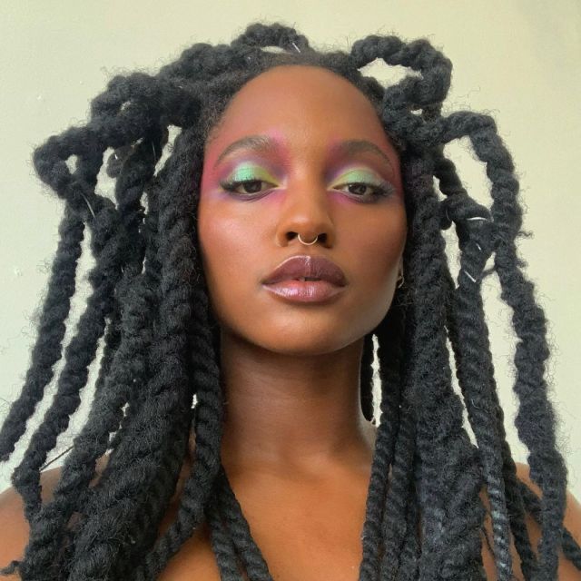 Mulher de pele preta, com cabelo preto com dread e maquiagem com sombra colorida
