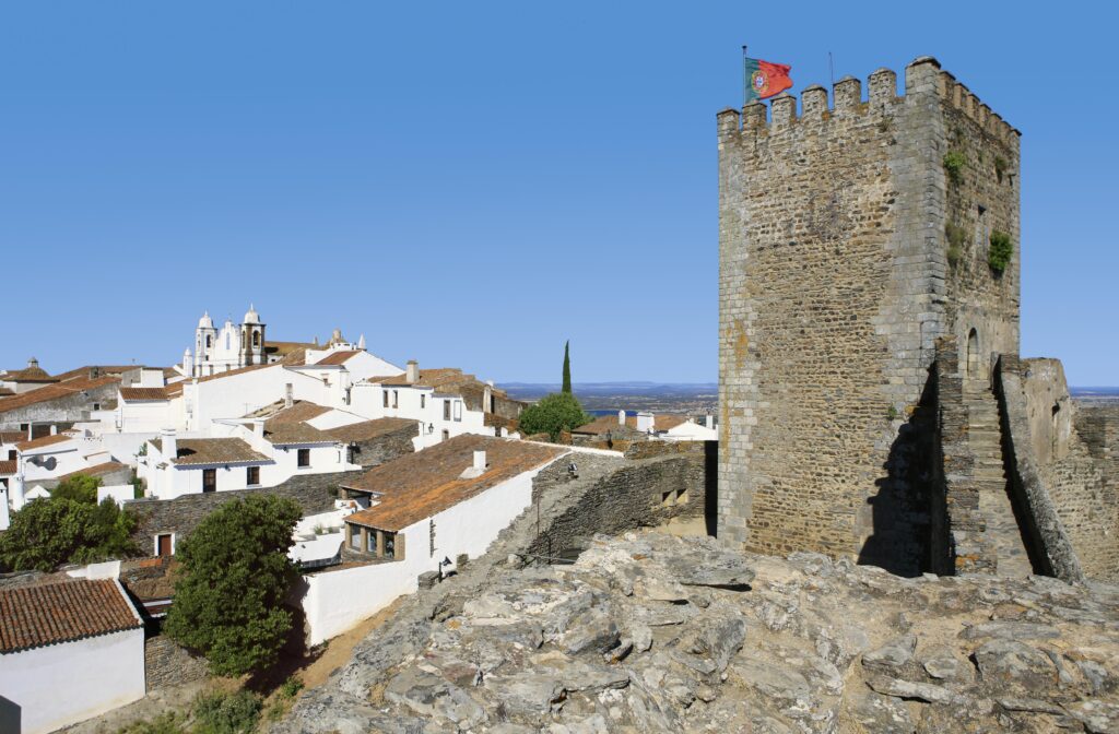Castelo no alto de uma colina e ao fundo casas brancas