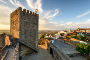 Castelo no alto de uma colina, céu azul e casas brancas