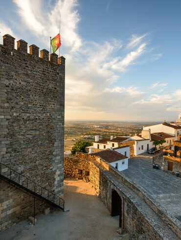 Castelo no alto de uma colina, céu azul e casas brancas