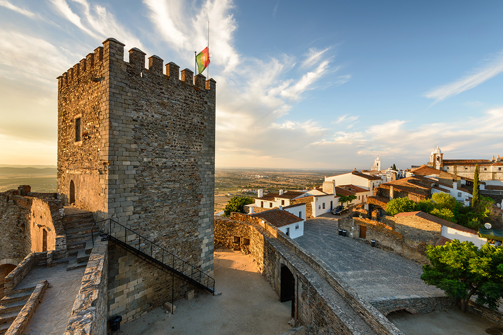 Castelo no alto de uma colina, céu azul e casas brancas