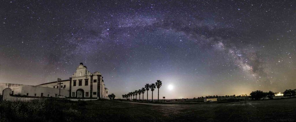 Lugar com arquitetura em concreto branca, algumas palmeiras e céu estrelado