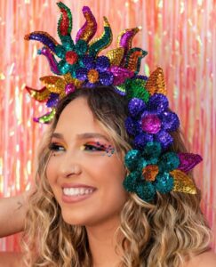 Mulher de pele clara, com cabelo loiro cacheado, acessório de cabeça de Carnaval e maquiagem colorida