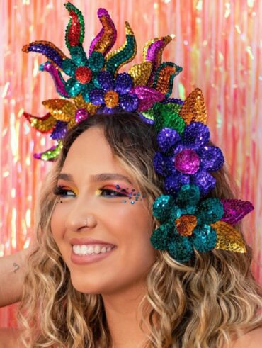 Mulher de pele clara, com cabelo loiro cacheado, acessório de cabeça de Carnaval e maquiagem colorida