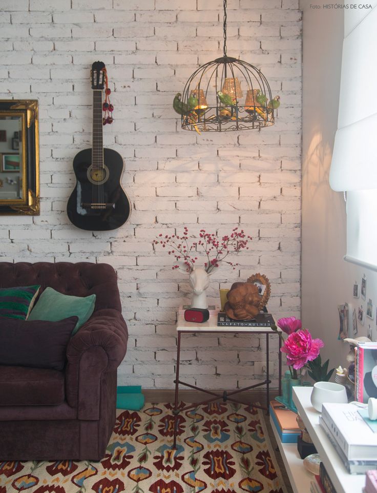 Sala com sofá de veludo, parede de tijolinhos brancos, violão pendurado, e tapete colorido