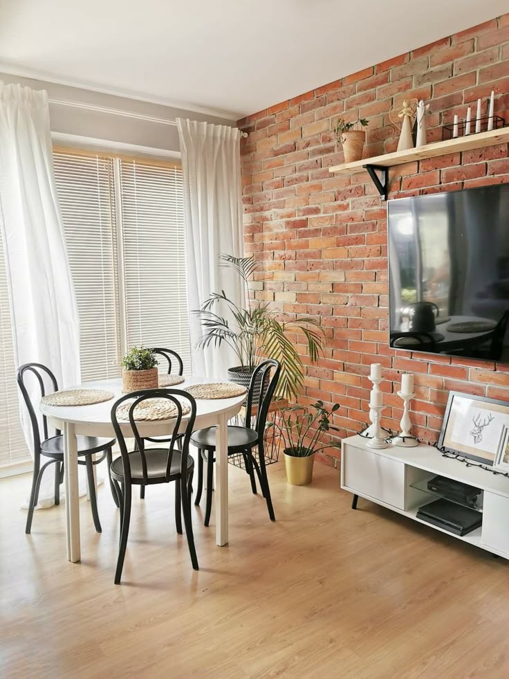 Sala de jantar com mesa branca e cadeiras pretas, rack branco e parede de tijolinhos