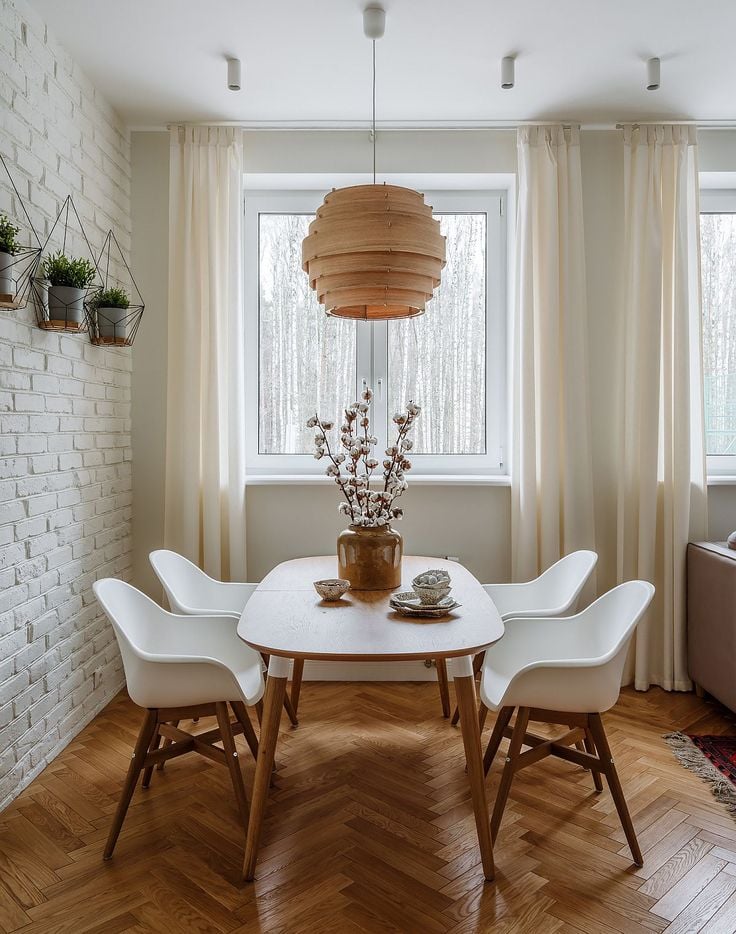 Sala de jantar branca e detalhes amadeirados, com mesa oval, parede de tijolinhos brancos