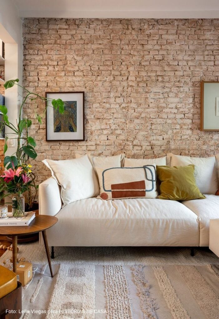 Sala de estar com sofá claro, parede de tijolinhos, quadros e mesa de canto