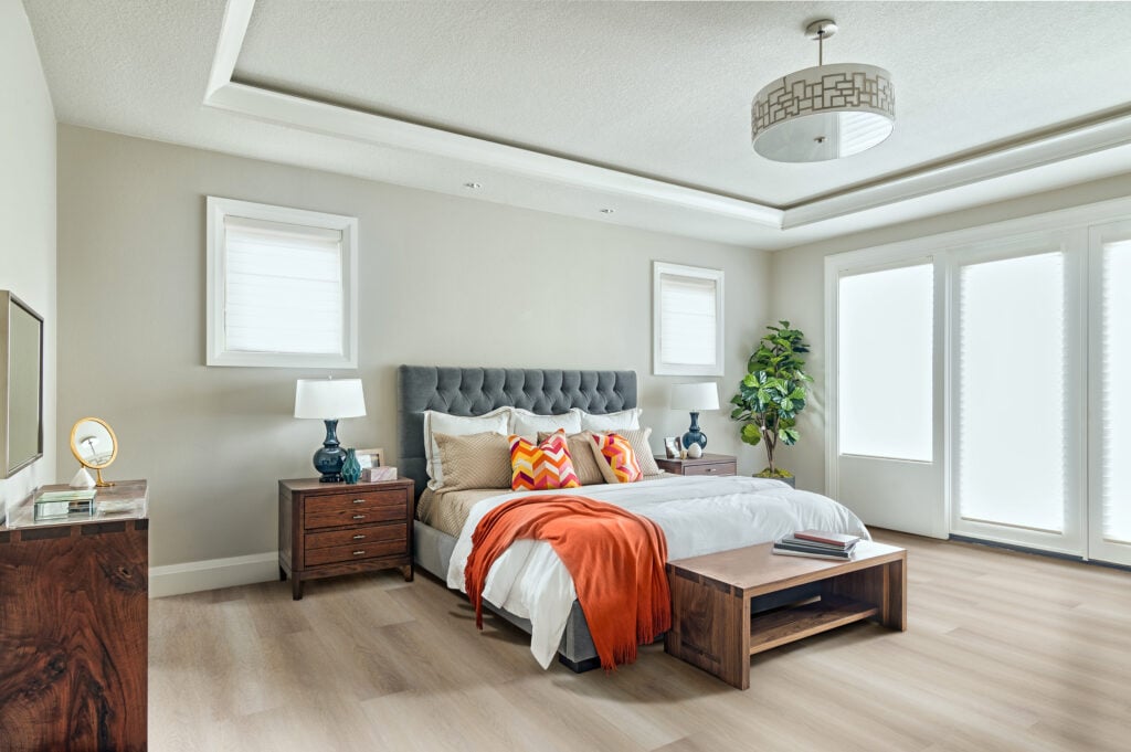 Quarto em tons neutros, com cama e cabeceira estofada cinza, banco e mesa de cabeceira de madeira