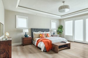 Quarto em tons neutros, com cama e cabeceira estofada cinza, banco e mesa de cabeceira de madeira