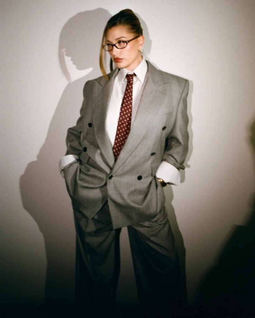 Hailey Bieber com blazer e calça de alfaiataria em cinza, camisa branca e gravata