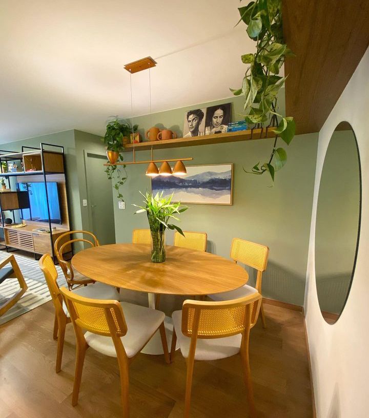 Sala de jantar com parede verde-claro, espelho redondo mesa e cadeiras em tom de amarelo