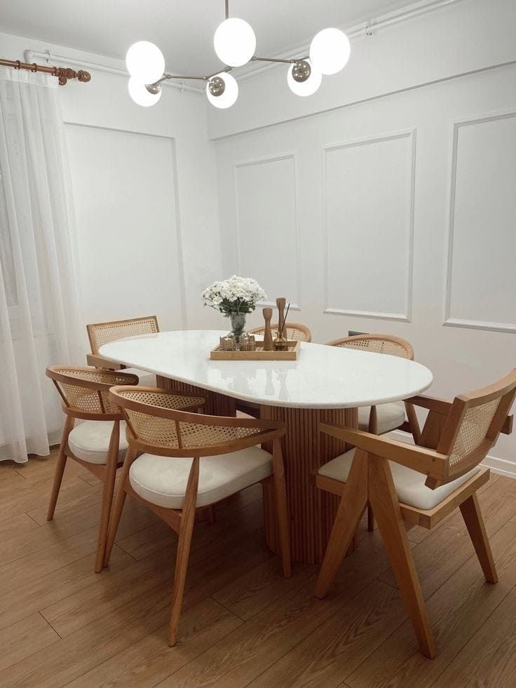 Sala de jantar com mesa oval e tampo claro, cadeiras de madeira com estofado neutro e encosto de palhinha