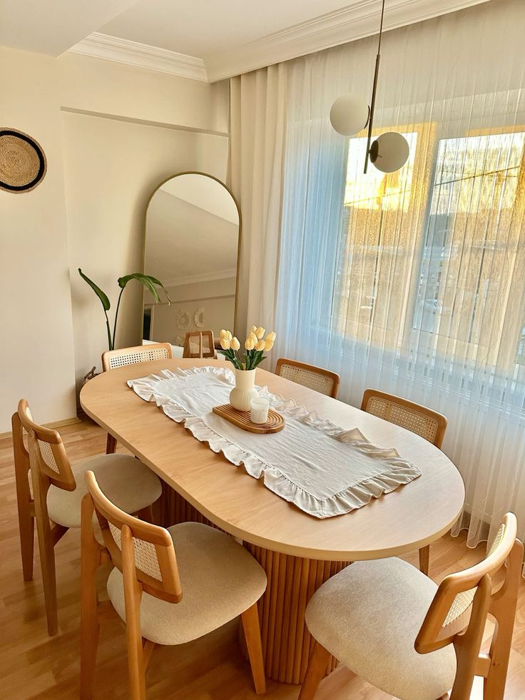 Sala de jantar com mesa oval de madeira, cadeiras de madeira com assento estofado e espelho oval no canto