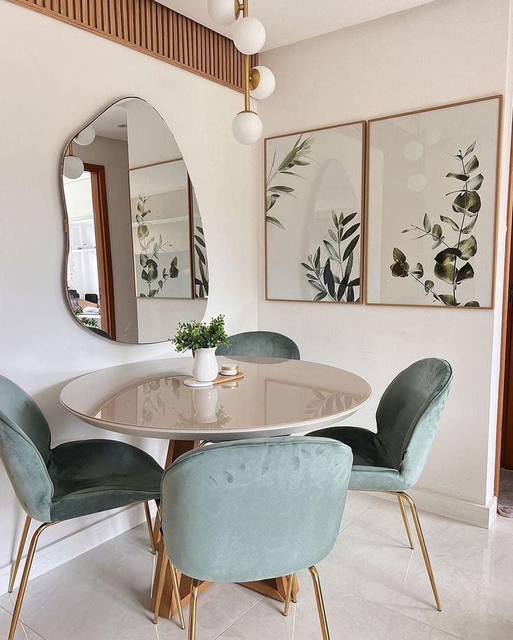 Sala de jantar com mesa redonda, cadeiras estofadas em veludo, espelho orgânico e quadros na parede