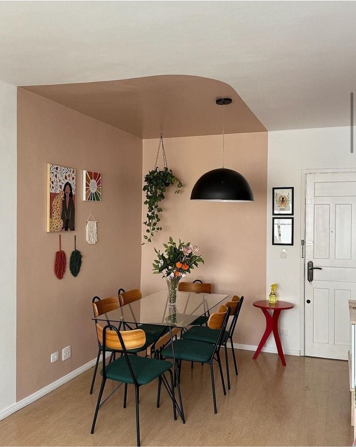 Sala de jantar com mesa de vidro, cadeiras com assento verde-escuro e quadrinhos na parede