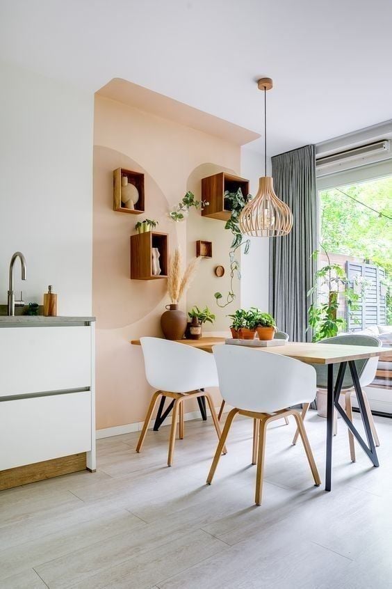 Sala de jantar em tons neutros, com mesa de madeira, cadeira com encosto branco e nichos de madeira na parede